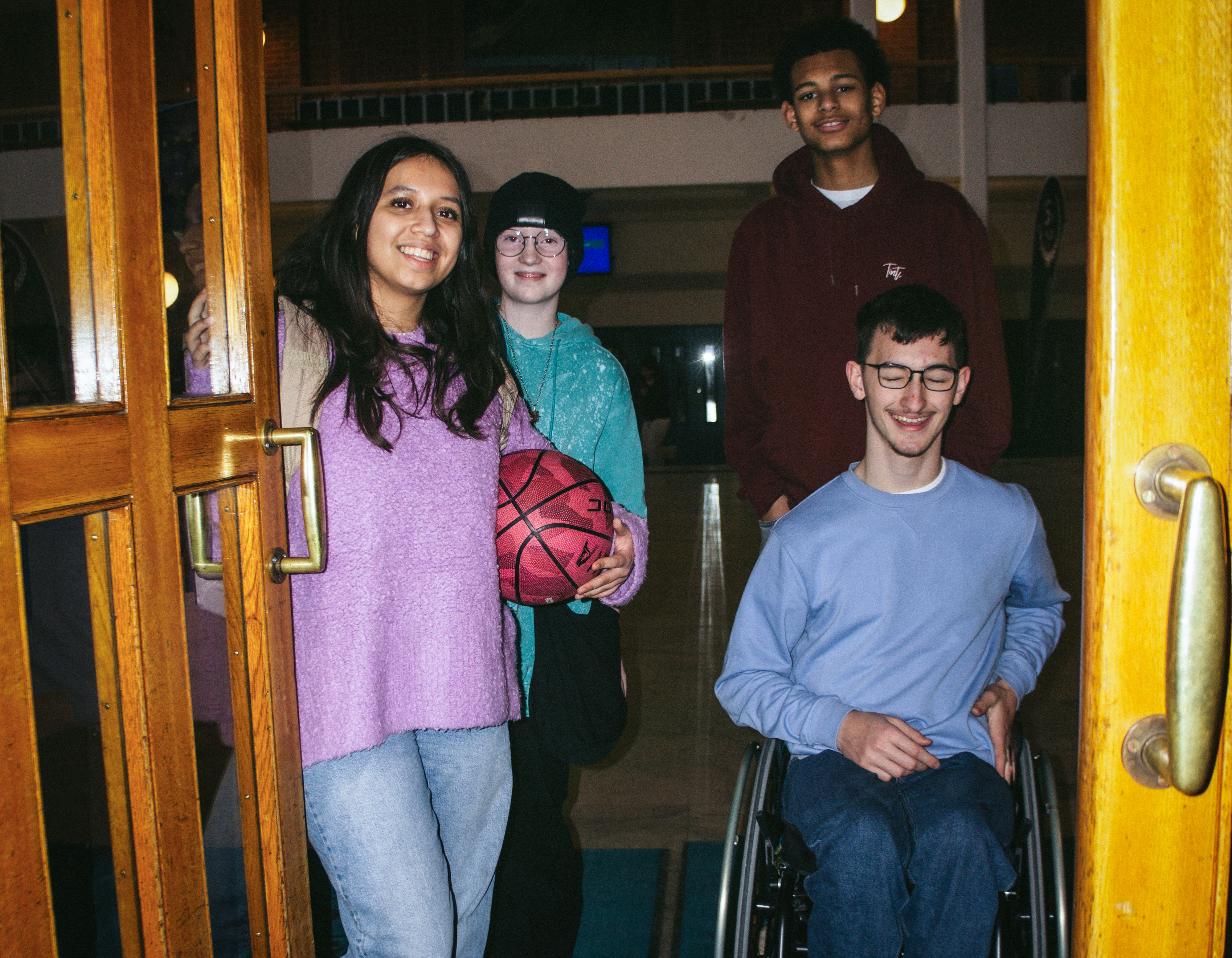Fyra elever står i entrén till en idrottssal, varav en är rullstolsburen.