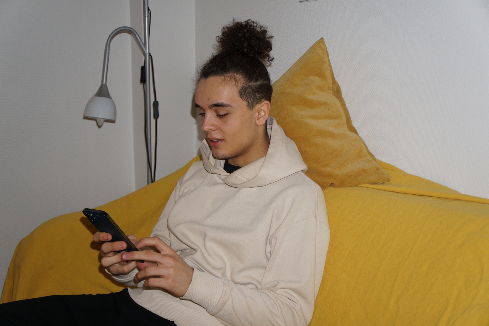 Ung person sitter i soffan med mobilen.
